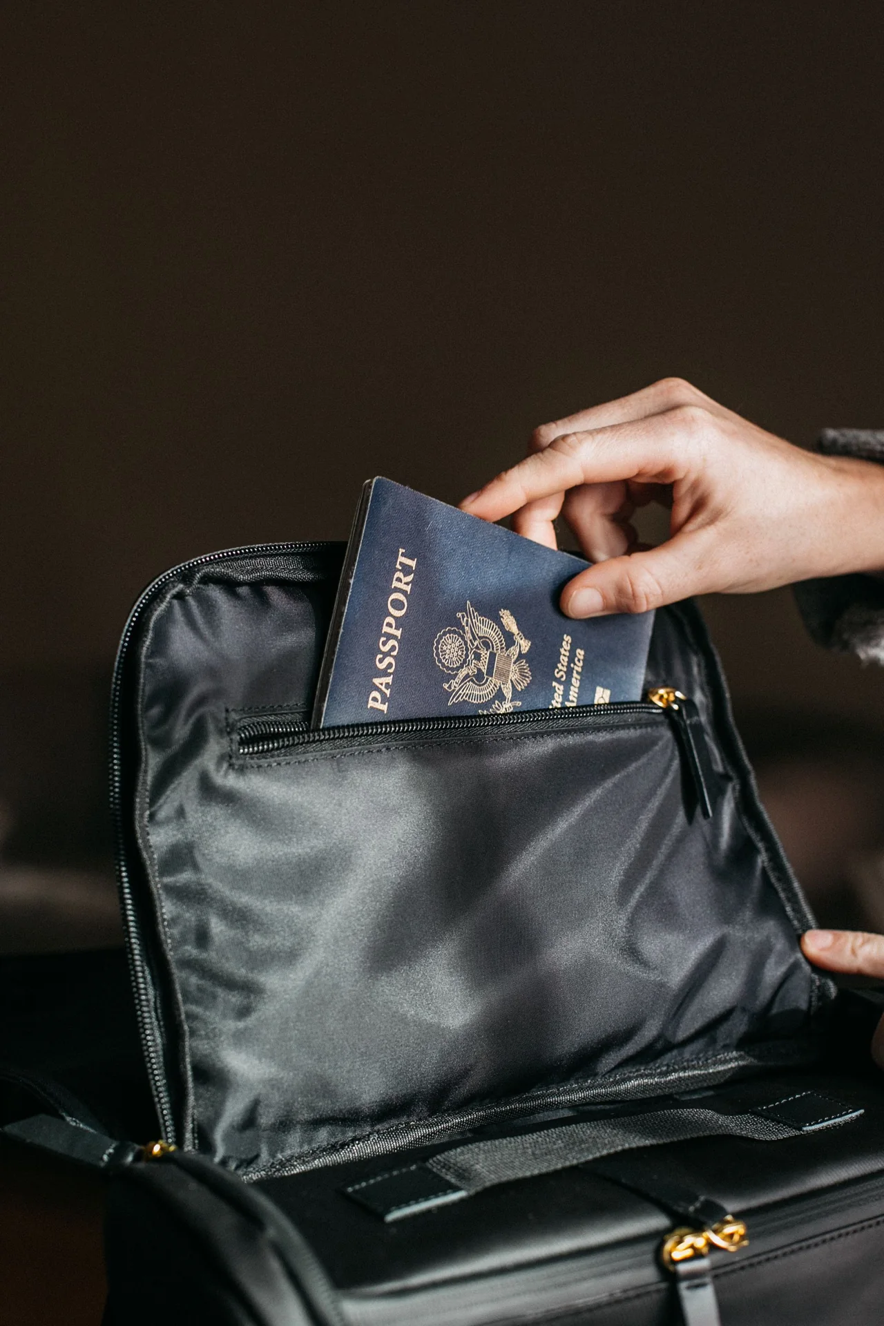 Tangan menyimpan pasport tertutup ke dalam beg perjalanan.